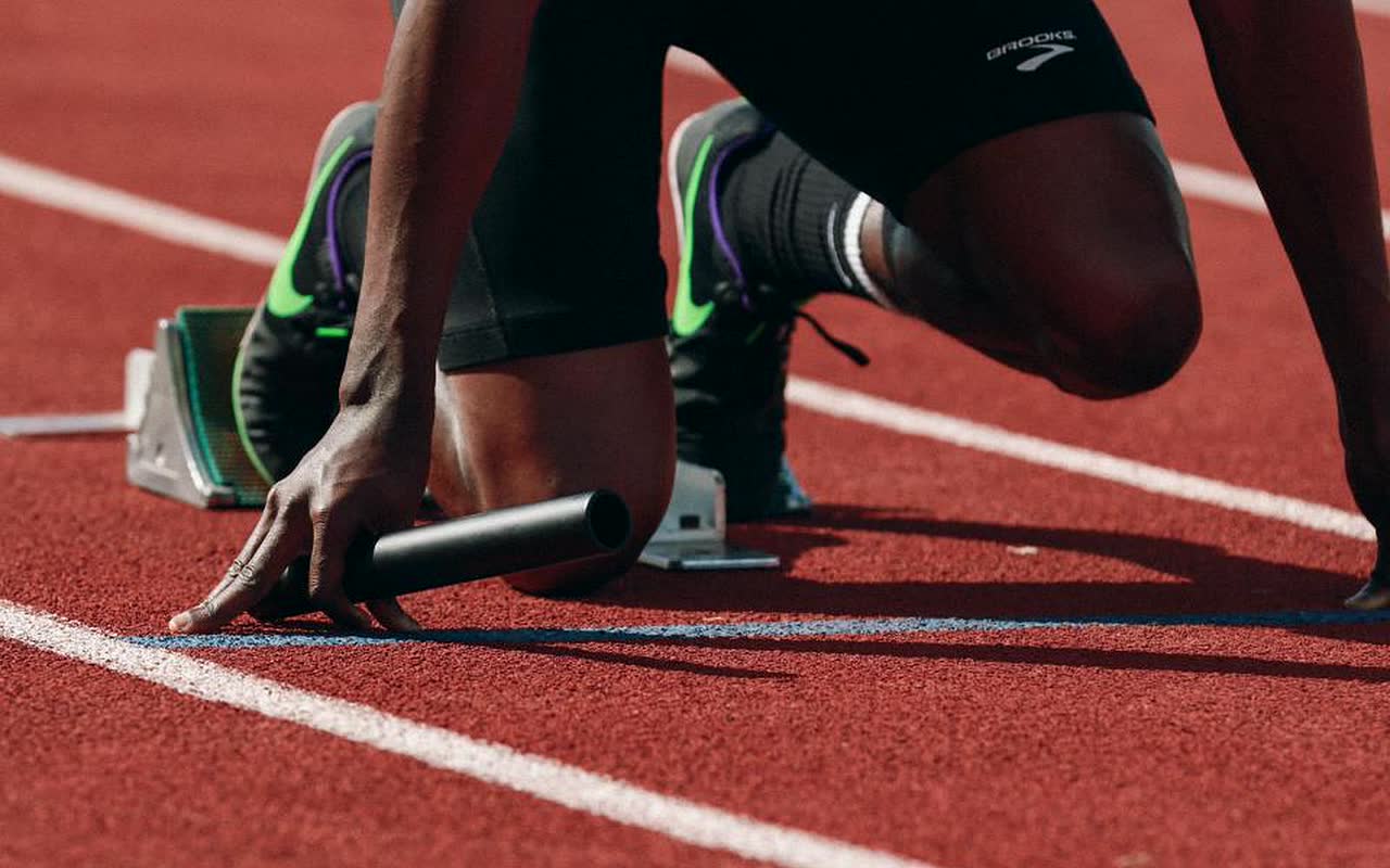 Velocista na saída dos blocos, em pista de atletismo vermelha